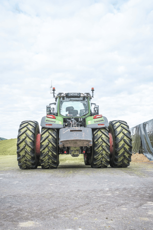 Tracteur agricole à quatre roues garé sur pavé sous un ciel nuageux.